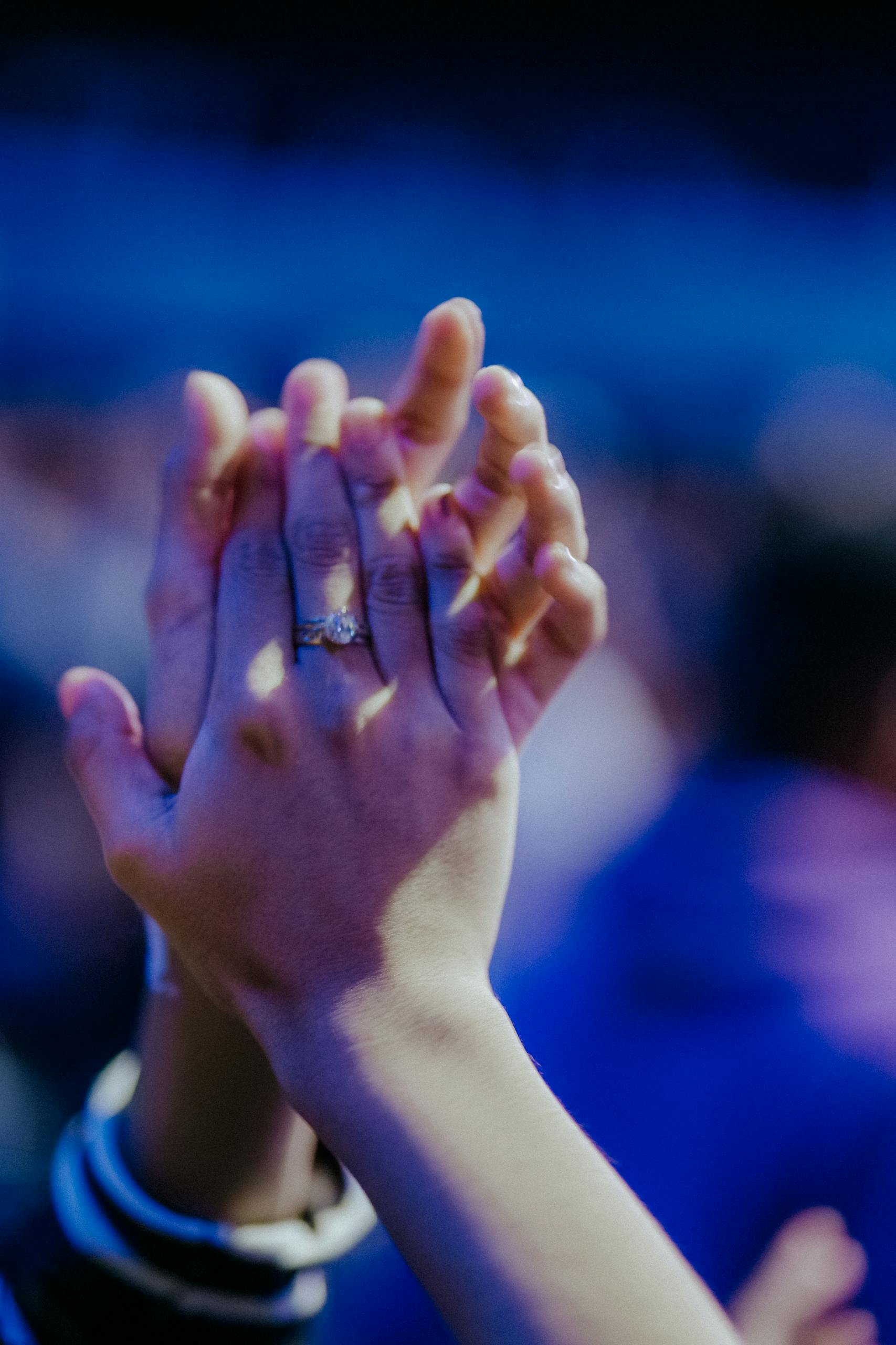 A vertical shot of intertwined hands clapping, highlighting a diamond ring.